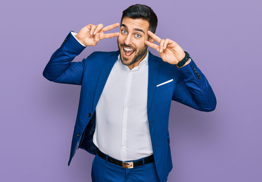 Young hispanic man wearing business jacket doing peace symbol with fingers over face, smiling cheerful showing victory