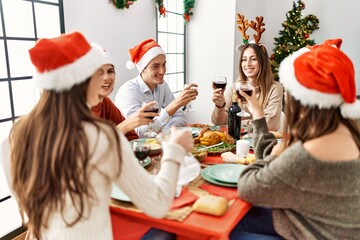 Group of young people smiling happy celebrating christmas eating and sitting on the table at home.