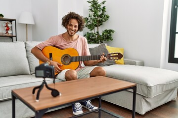 Young hispanic man recording with camera playing classical guitar at home.