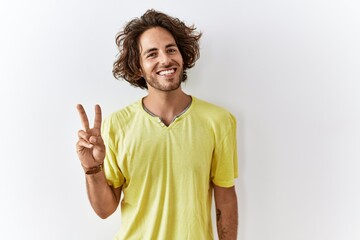 Young hispanic man standing over isolated background showing and pointing up with fingers number two while smiling confident and happy.