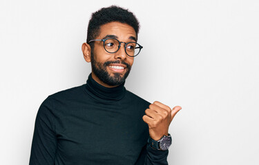 Young african american man wearing casual clothes smiling with happy face looking and pointing to the side with thumb up.