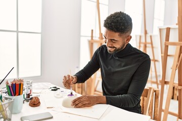 Young african american artist man smiling happy painting pottery at art studio.