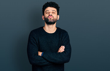 Young arab man with beard with arms crossed gesture looking at the camera blowing a kiss being...