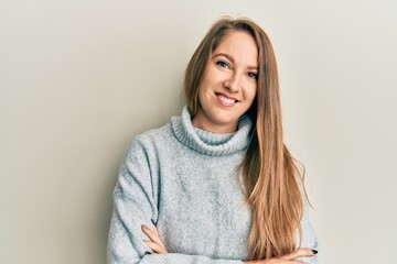 Young blonde woman wearing casual turtleneck sweater happy face smiling with crossed arms looking at the camera. positive person.