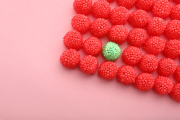 Delicious green gummy raspberry candy among red ones on pink background, flat lay. Space for text