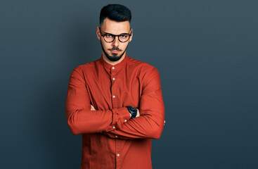 Fototapeta premium Young hispanic man with beard wearing business shirt and glasses skeptic and nervous, disapproving expression on face with crossed arms. negative person.