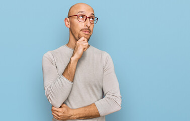 Bald man with beard wearing casual clothes and glasses with hand on chin thinking about question,...