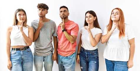 Group of young friends standing together over isolated background thinking concentrated about doubt with finger on chin and looking up wondering