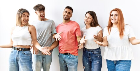 Fototapeta premium Group of young friends standing together over isolated background smiling cheerful with open arms as friendly welcome, positive and confident greetings