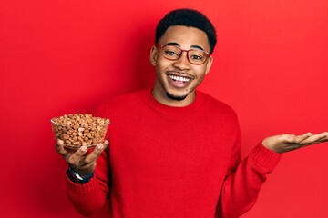 Young african american man holding peanuts celebrating achievement with happy smile and winner expression with raised hand