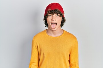 Handsome young man wearing wool hat sticking tongue out happy with funny expression. emotion concept.