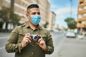 Young latin tourist man wearing medical mask using camera at the city.