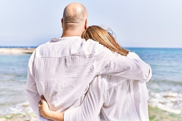 Middle age hispanic couple of husband and wife together walking by the beach on a sunny day. Hugging in love on vacation to the seaside.