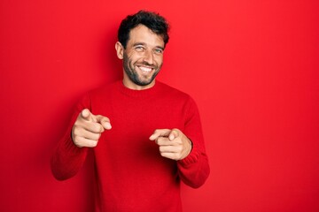 Handsome man with beard wearing casual red sweater pointing fingers to camera with happy and funny...
