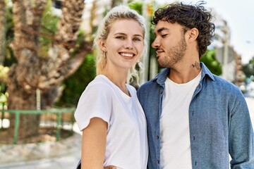 Obraz premium Young beautiful couple of caucasian girlfriend and hispanic boyfriend hugging in love outdoors on a sunny day. Woman and man smiling happy dating relationship