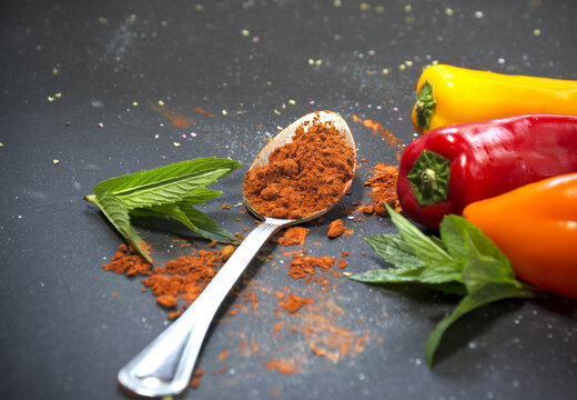 Red paprika powder in tablespoon with bell papers on a black background