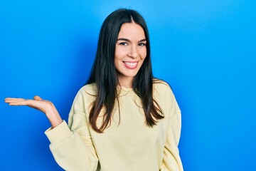 Young brunette woman wearing casual sweatshirt smiling cheerful presenting and pointing with palm of hand looking at the camera.