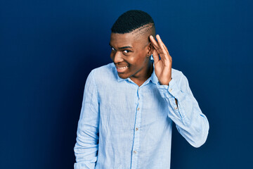 Young african american man wearing casual clothes smiling with hand over ear listening an hearing to rumor or gossip. deafness concept.