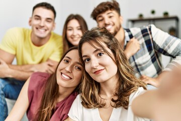 Group of young friends smiling happy make selfie by the smartphone sitting on the sofa at home.