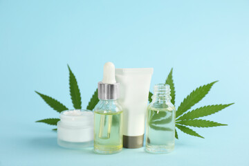 Cream, hemp leaves, bottles of CBD oil and THC tincture on light blue background