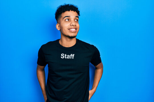 Young african american man wearing staff t shirt smiling looking to the side and staring away thinking.