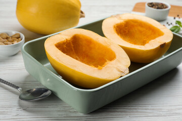 Raw spaghetti squash halves in baking dish on white wooden table, closeup