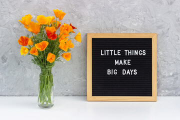 Little things make big days. Motivational quote on letter board and bouquet orange flowers on white table against grey stone wall. Concept inspirational quote of the day