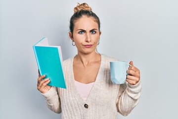 Beautiful caucasian woman with blond hair reading a book and drinking a cup of coffee skeptic and nervous, frowning upset because of problem. negative person.