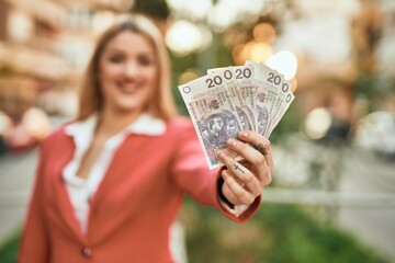 Young blonde businesswoman smiling happy holding polish zloty at the city.