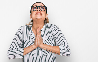 Young caucasian woman wearing business shirt and glasses begging and praying with hands together...