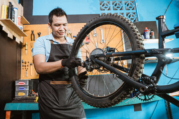 Fototapeta na wymiar bicycle mechanic in aprons tightens spokes while fixing problems on bicycles in a workshop