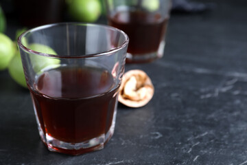 Delicious liqueur and fresh walnuts on black table, closeup. Space for text