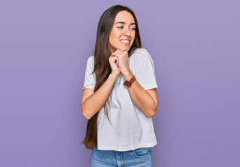 Young hispanic girl wearing casual white t shirt laughing nervous and excited with hands on chin looking to the side