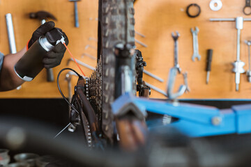 close up of a mechanic's hand wearing gloves using chain lube lubricating the chain and freewheel on a workshop background