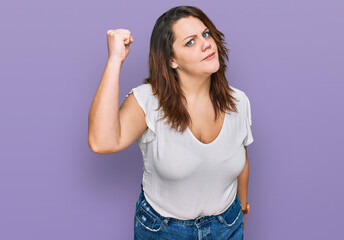 Young plus size woman wearing casual white t shirt angry and mad raising fist frustrated and furious while shouting with anger. rage and aggressive concept.