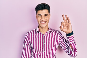 Young hispanic man wearing casual clothes smiling positive doing ok sign with hand and fingers. successful expression.