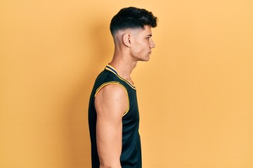 Young hispanic man wearing basketball uniform looking to side, relax profile pose with natural face with confident smile.