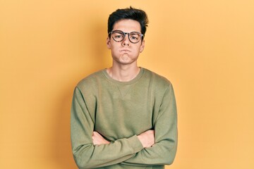 Young hispanic man with arms crossed gesture puffing cheeks with funny face. mouth inflated with air, catching air.