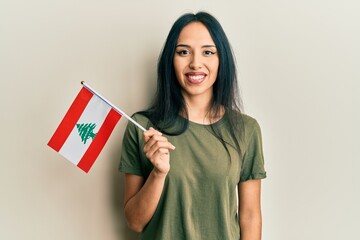 Young hispanic girl holding lebanon flag looking positive and happy standing and smiling with a...