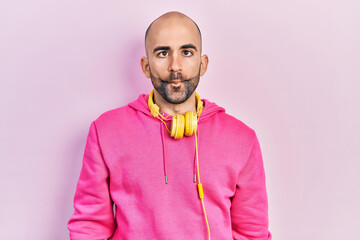 Young bald man wearing gym clothes and using headphones making fish face with lips, crazy and comical gesture. funny expression.