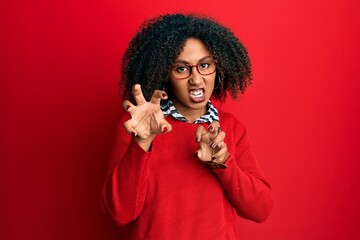 Beautiful african american woman with afro hair wearing sweater and glasses smiling funny doing claw gesture as cat, aggressive and sexy expression