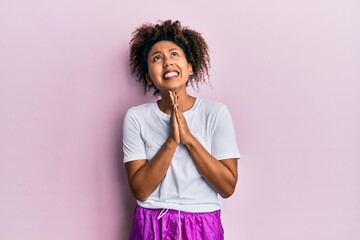 Beautiful african american woman with afro hair wearing sportswear begging and praying with hands...