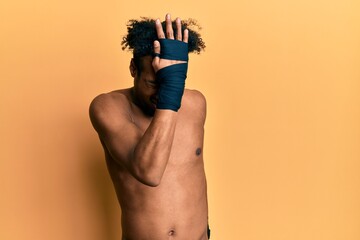 Young african american man with beard using boxing protection surprised with hand on head for...