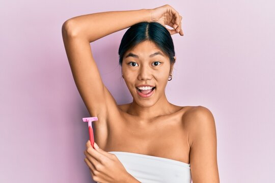 Young chinese woman wearing shower towel using razor celebrating crazy and amazed for success with open eyes screaming excited.