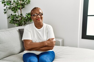 Mature hispanic woman sitting on the sofa at home smiling looking to the side and staring away thinking.