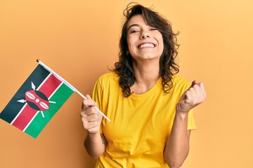 Young hispanic woman holding kenya flag screaming proud, celebrating victory and success very excited with raised arm