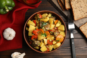 Tasty cooked dish with potatoes in earthenware served on wooden table, flat lay
