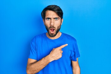 Young hispanic man wearing casual clothes surprised pointing with finger to the side, open mouth amazed expression.