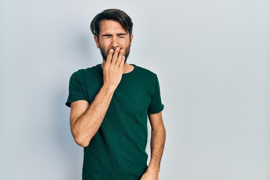 Young hispanic man wearing casual white tshirt bored yawning tired covering mouth with hand. restless and sleepiness.