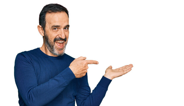 Middle age hispanic man wearing casual clothes amazed and smiling to the camera while presenting with hand and pointing with finger.